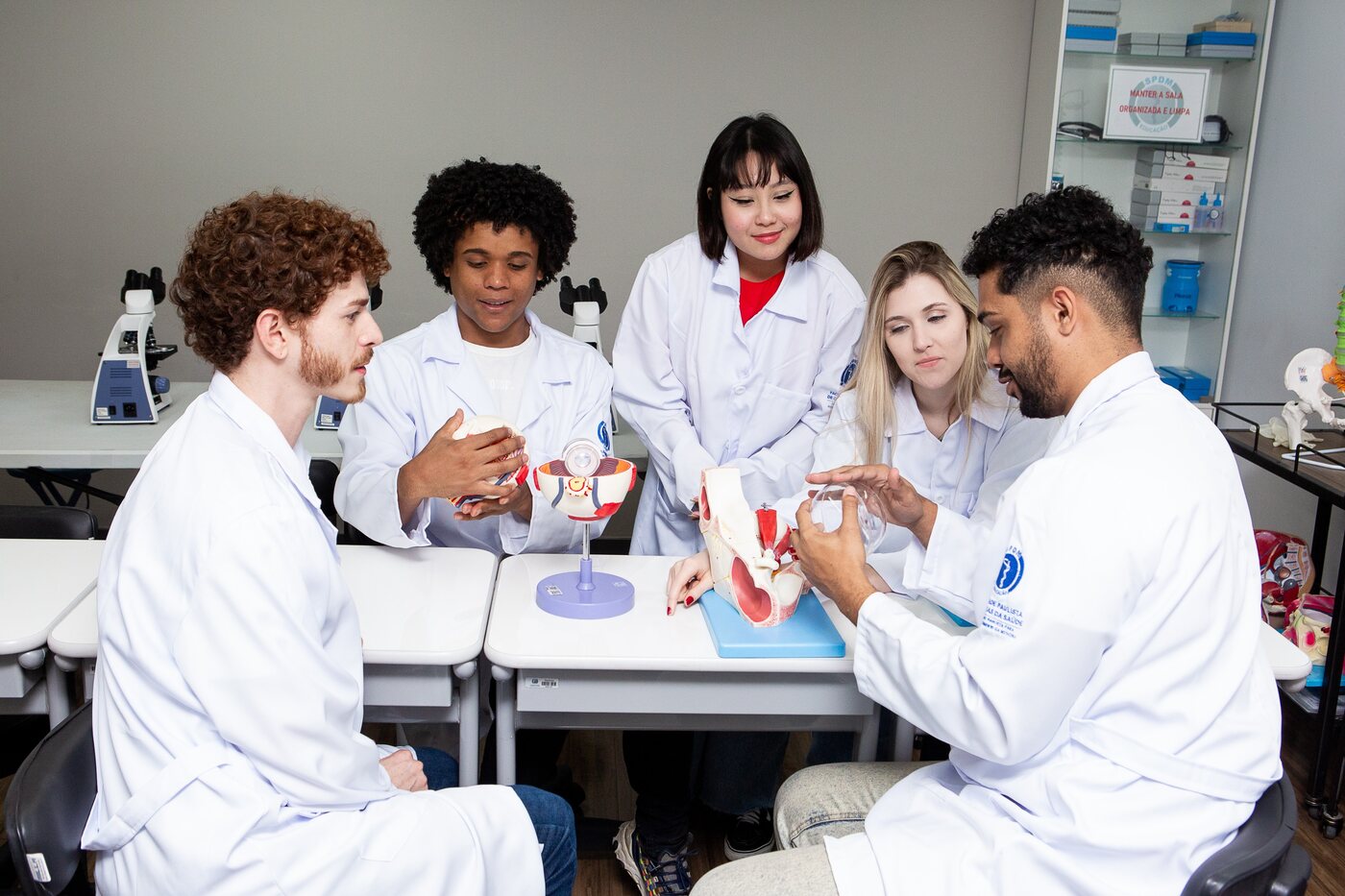 Estudantes de jaleco em prática de laboratório com microscópio e modelo anatômico